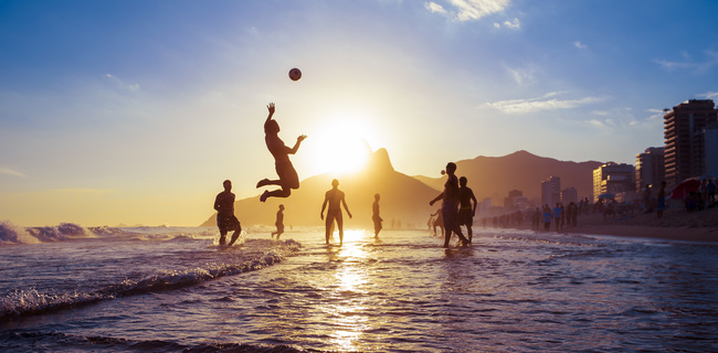 sunset silhouettes playing keepy-uppie beach football on the sea shore in Ipanema Beach Rio de Janeiro Brazil